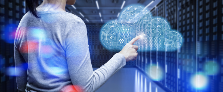 A person in a data center interacts with a holographic cloud icon, symbolizing cloud infrastructure management. The background shows rows of servers, highlighting the integration of cloud technology in modern data management. The image represents the monitoring, maintaining, and optimizing of cloud-based infrastructure for seamless operations.