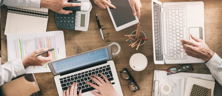 A group of professionals working on laptops and tablets, discussing data protection in New York, cybersecurity strategies, and secure business operations.