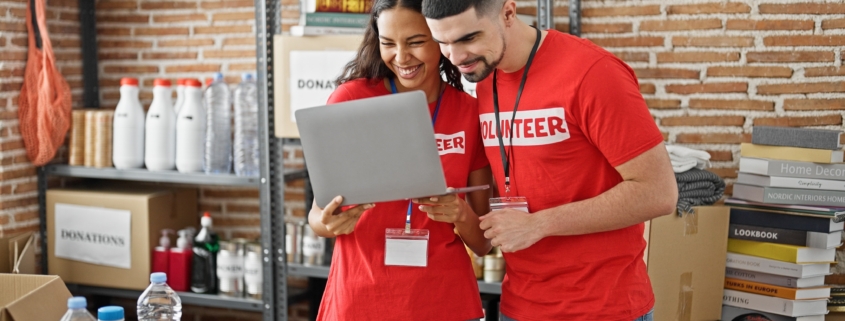 Two volunteers in a donation center smiling at a laptop, illustrating how nonprofits benefit from managed IT services in New York City to stay connected, efficient, and secure.