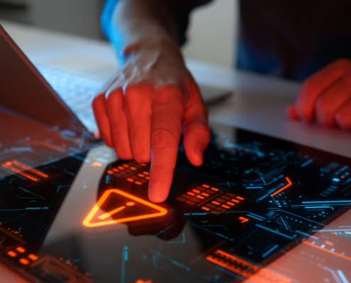 Close-up of a person's hand interacting with a futuristic touchscreen interface displaying a warning symbol and digital data, symbolizing threat detection and system monitoring — representing advanced cyber risk management in New York.