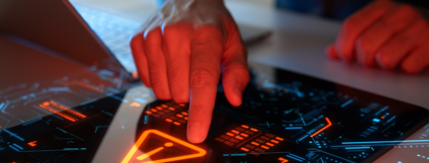 Close-up of a person's hand interacting with a futuristic touchscreen interface displaying a warning symbol and digital data, symbolizing threat detection and system monitoring — representing advanced cyber risk management in New York.